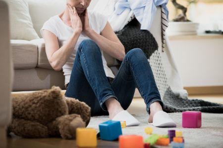 Overwhelmed military spouse mom sitting on floor surrounded by toys