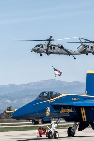 helicopter with american flag in tow flying over blue angel plane